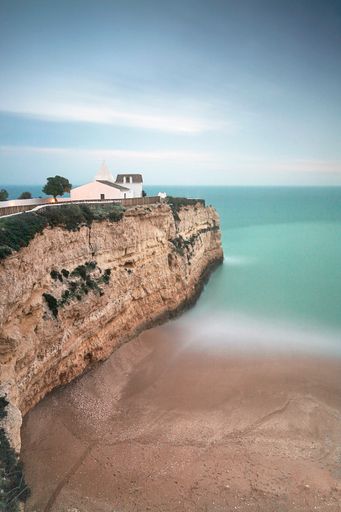An aerial, vertical shot of a wavy beach surrounded by rocks and cliffs, Algarve, Portugal