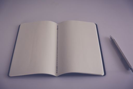 A high angle shot of the desk of a poet with an open notebook and a silver pen on a white surface