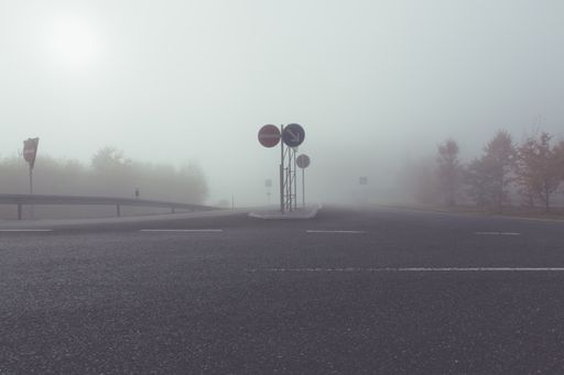 A low angle shot of two street signs on the empty road with the fog in the background
