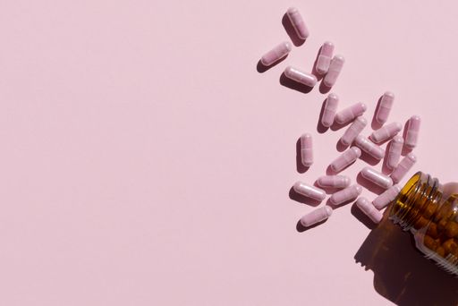 A high angle shot of pink capsules scattered from a bottle of pills on a pink surface