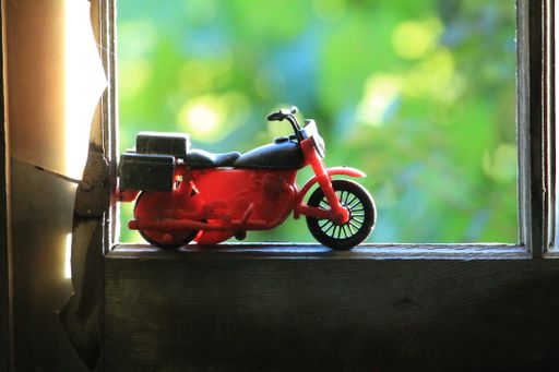A shallow focus of a motocycle bike toy on a window with blurred green trees in the background