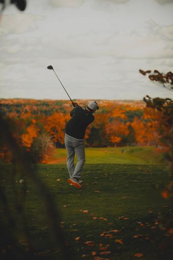 A rear view of a male golfer playing on a field against autumnal forest