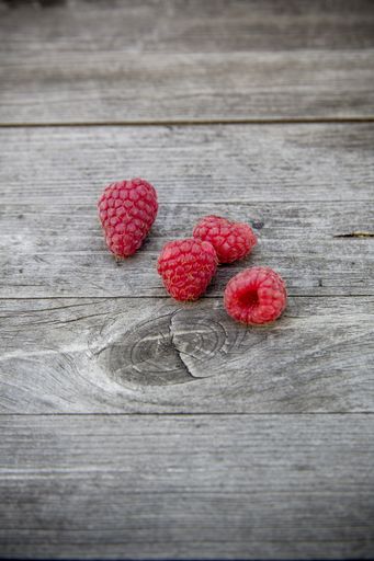A closeup shot of four raspberries on a wooden surface