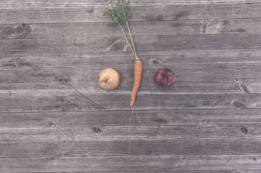 A high angle shot of a carrot and two onions on a wooden surface