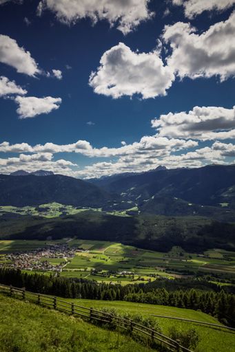 A beautiful vertical shot of green land and mountains under the breathtaking cloudy sky at daytime