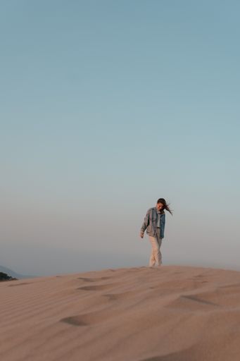 Desert adventure. Young woman  walking on sand dunes, windy weather