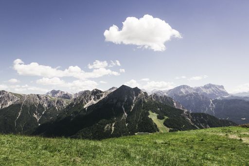 A wide shot of a green mountain in the field of grass with the background of cloudy sky