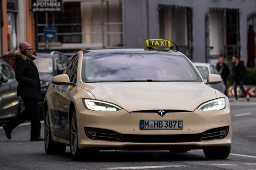 A white electric Tesla taxi cab on the street in Munich during the daytime