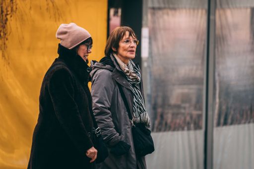 Two senior women in winter clothes walking on a street and talking to each other