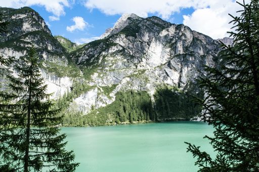 A scenic shot of a beautiful body of water surrounded by rocky mountains and green trees under the cloudy sky