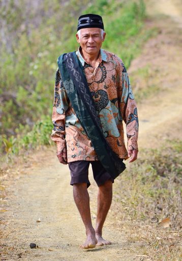 A vertical closeup of the old man in traditional clothes walking along the rural path. PalopoIndonesia