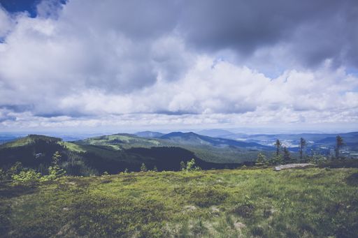 A wide shot of beautiful green mountains and trees under the breathtaking cloudy sky