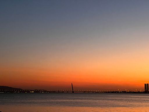 A mesmerizing shot of a sunset opening from the sea with a pretty view of the city