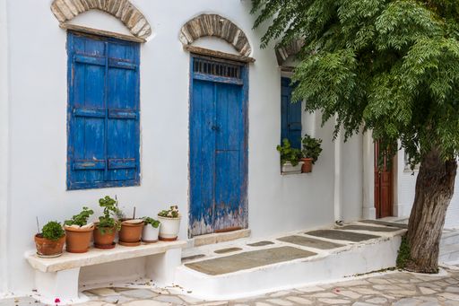 A closeup of blue wooden windows and a door of an old white house in Pyrgos, Greece
