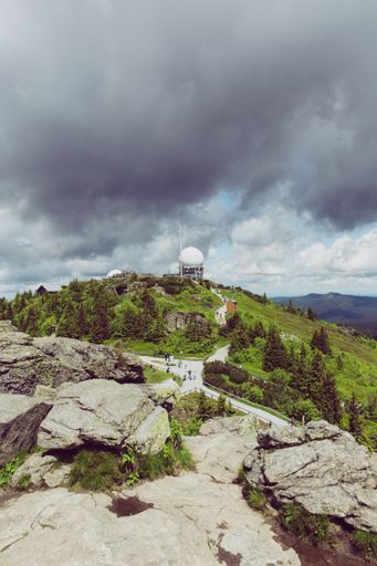 A vertical shot of huge rocks and green pine trees under the cloudy sky