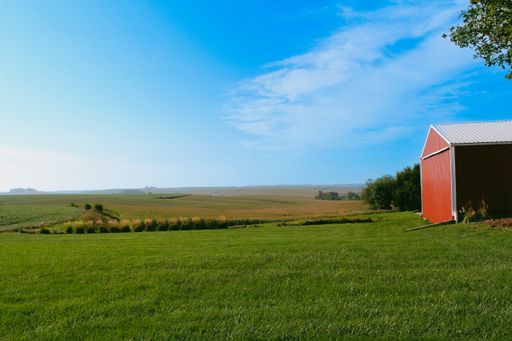A green farm and a red barn in Iowa under a blue cloudy sky on a sunny day