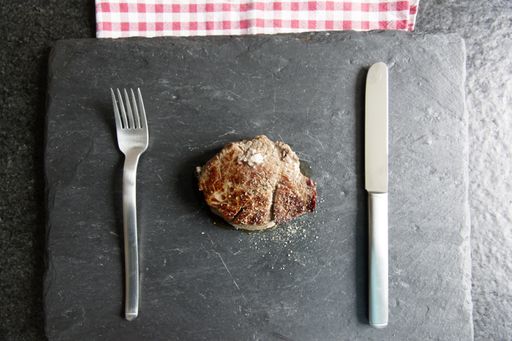 A high angle shot of a piece of tasty steak with a fork and a knife