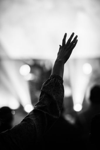 A grayscale of a female pointing her hand up with a blurry background of concert lights
