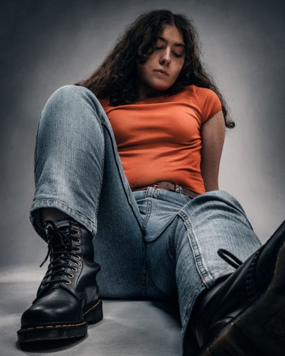 A vertical shot of a woman sitting on the ground wearing black boots and an orange top