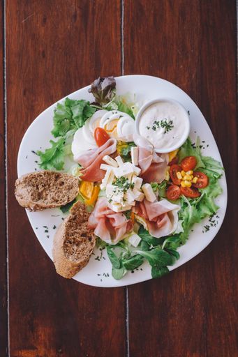 A vertical shot of a salad with cheese, prosciutto, eggs and bread