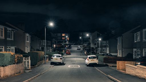 A night view of British suburban street surrounded by cars and buildings at night