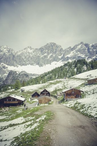 A vertical shot of wooden houses on the mountains covered in snow in wintertime under the crazy sky