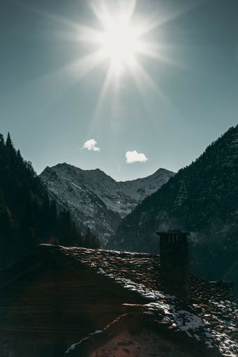 A vertical sot of a small house surrounded by rocky mountains covered in the snow in the countryside