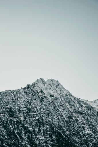 A vertical shot of rocky mountains covered in the snow and trees under a cloudy sky