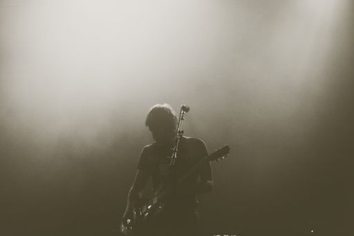 A greyscale shot of an artist playing electric guitar on stage during a concert with a smokey background