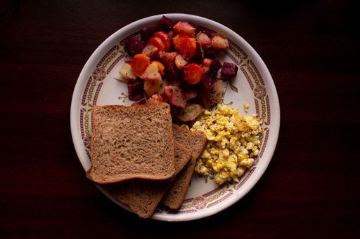 A top view of wheat bread slices with scrambled eggs and fresh salad on a plate on the table