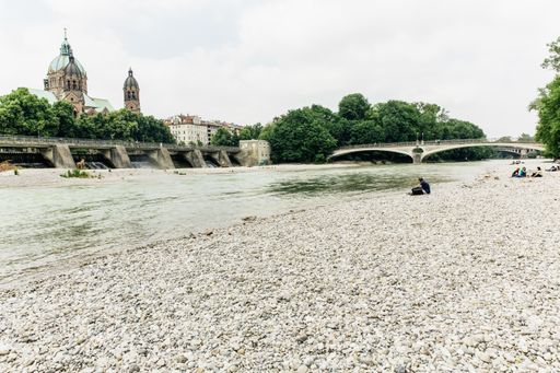 A low angle shot of a beautiful beach with a bridge surrounded by high buildings and green trees