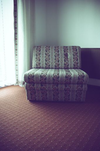 A vertical shot of a couch with flowers in a room with white curtains and red carpet