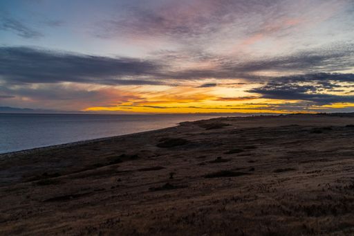A landscape of a lake under a cloudy sky during the sunset in the evening