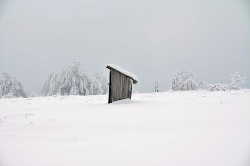 An old toilet on a snowy field with the grey sky in the background