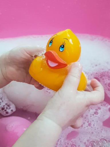 A closeup shot of a baby playing with a yellow duck in a pink bathtub