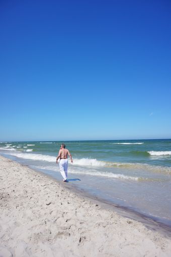 A vertical shot of a man walking on the sand near the beach in summer
