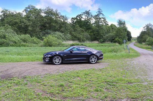 Black Ford Mustang V8 sports car in front of a northern germany landscapes on a sunny day.