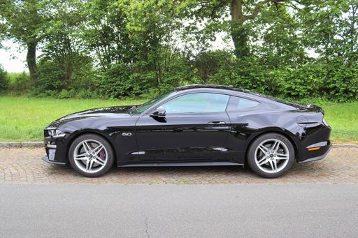 Black Ford Mustang V8 sports car in front of a northern germany landscapes on a sunny day.
