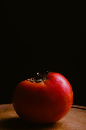 A vertical closeup shot of fresh tomato on a wooden surface on a black background