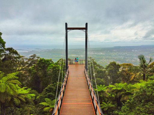 A beautiful view of a couple on a high wooden bridge with fence and trees leading to the city