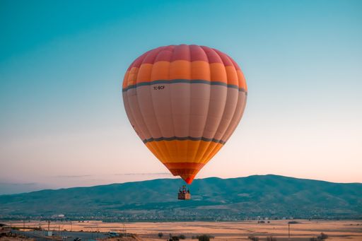 A scenic view of an orange hot air balloon in the blue sky against mountains