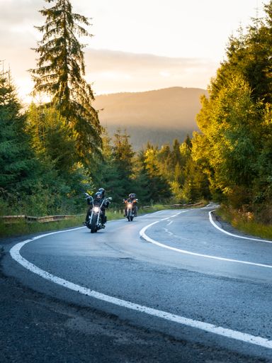 A vertical shot of two motorcycles driving on an asphalt road