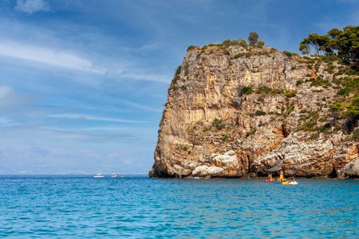 A beautiful view of rocky high form on the blue water sea against a blue sky in San Vito Lo Capo, Zingaro Nature Reserve