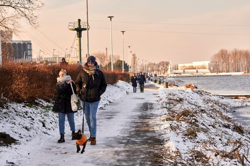 A woman and man walking with their dog on a footpath with snow and ice next to a lake in the Malta park.