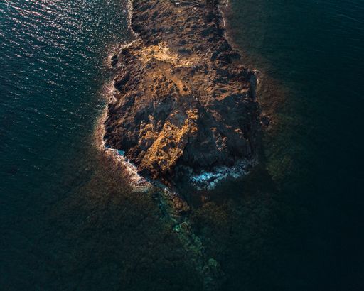 A bird's eye view of a rock peninsula being washed by ocean waves