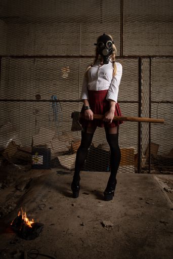 Woman wearing casual clothing and gas protective mask holding axe in an underground warehouse