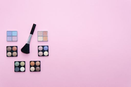 Make-up set with various colors and a brush on pink background. Beauty concept, copy space