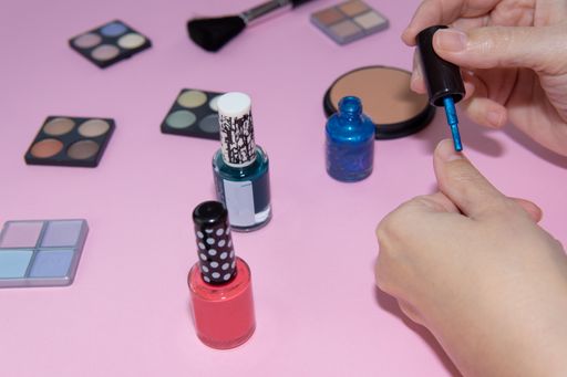 Close up Woman's hands painting her nails with blue nail polish. Cosmetic set on pastel pink background. Beauty concept, copy spac