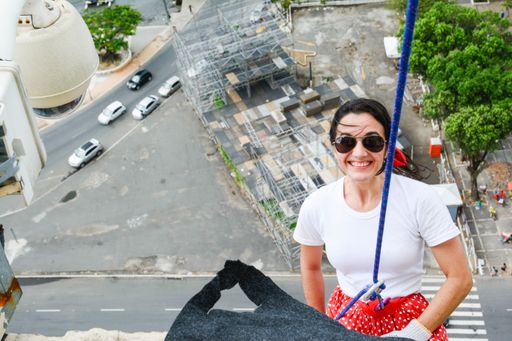 A happy caucasian woman tied from a rope descending from a tall building in a hero costume