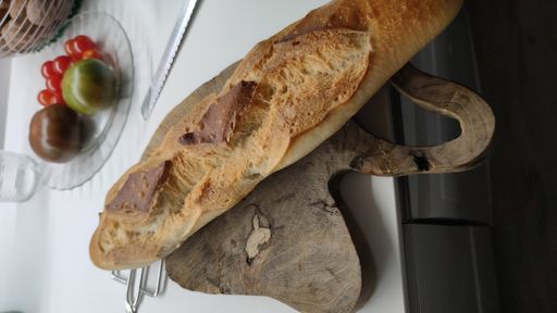 A vertical shot of a baguette bread on the wooden board near some vegetables